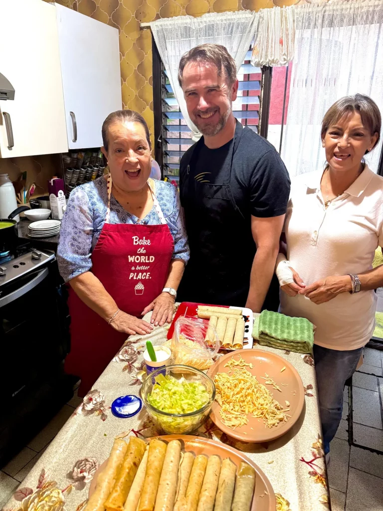 American Retiree taking part in a Mexican cooking class, smiling next to the old female chef, in Cuernavaca Mexico